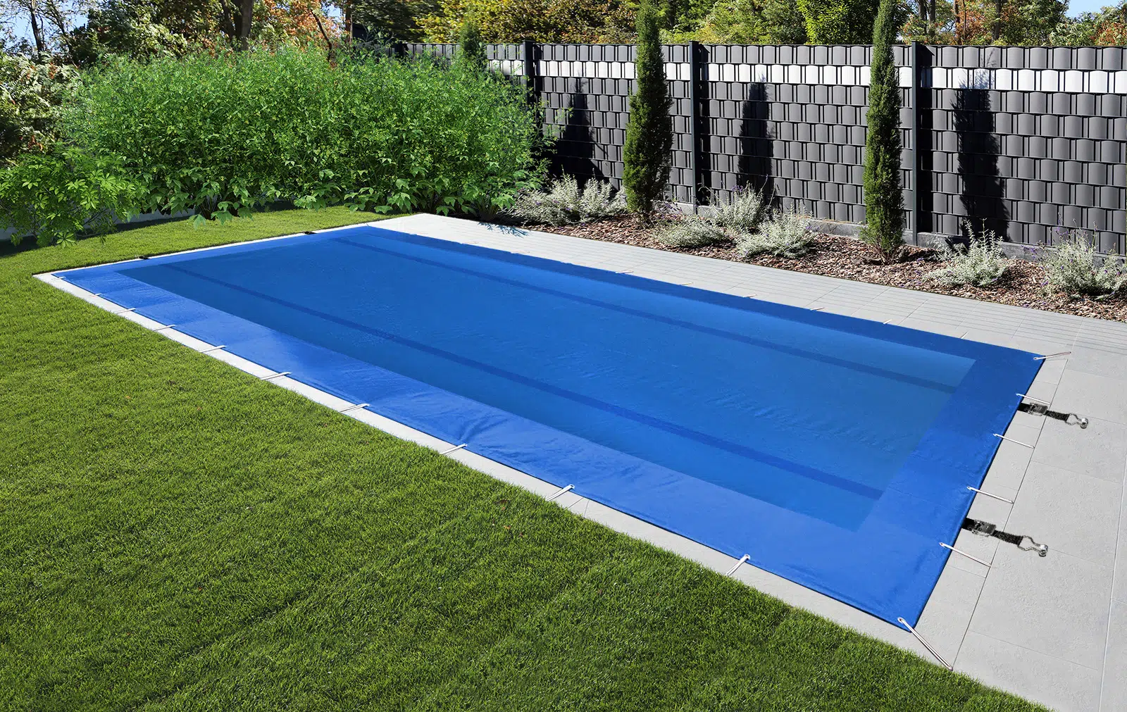 Ein mit einer blauen Plane abgedeckter Pool ist von Gras und grauen Steinfliesen umgeben, im Hintergrund sind hohe Pflanzen und ein moderner schwarzer Stabilisierungsgurtzaun zu sehen.