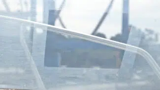 Eine verschwommene Außenreflexion erscheint auf einem schmutzigen, zerkratzten Glasfenster - ideal für die Reinigung mit Vuplex Kunststoffreiniger (Klarsichtfolien-Reiniger) -, das von einem weißen diagonalen Geländer durchzogen ist.