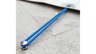 Nahaufnahme eines blauen Gummiseils, das an einer Metallöse auf einer grauen Plane befestigt ist, die auf Stein liegt. Der Versenkbare Bodenanker aus Edelstahl -12mm- hält das leicht gespannte Seil an Ort und Stelle.