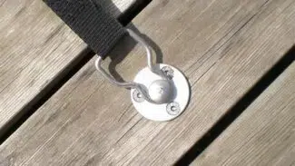 Ein Versenkbarer Bodenanker aus Edelstahl (12 mm) wird mithilfe von Schrauben sicher auf einer verwitterten Holzoberfläche befestigt, wodurch die natürliche Maserung und Struktur hervorgehoben wird.