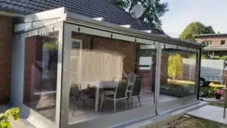 Eine Terrasse mit Carport- oder Terrassenplane – mit 1x Fenster/ohne Tür verfügt über transparente Vinylvorhänge, die einen Sitzbereich im Freien umschließen, der an ein Backsteinhaus mit grauem Dach angeschlossen ist, umgeben von Bäumen und einem in der Nähe geparkten LKW.