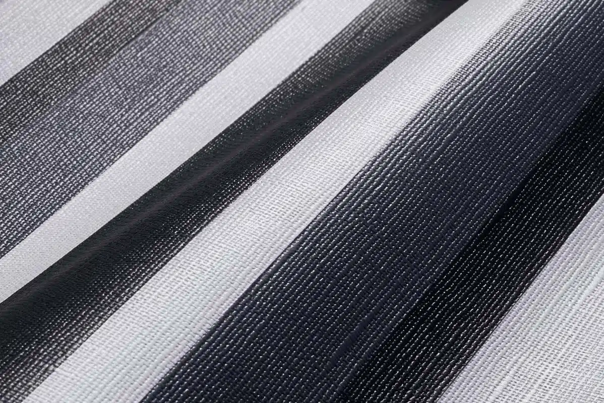 Nahaufnahme des MEHGIES® VALMEX® Solera Vorzeltplane-Stoffes mit vertikalen schwarzen, grauen und weißen Streifen. Die gewebte Textur und die Schattierungen erzeugen einen subtilen Farbverlaufseffekt.