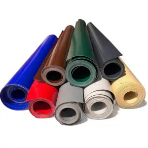 Gerollte LKW-Planenreste 450-950g/m² in Blau, Rot und Grau sind kunstvoll pyramidenförmig auf einem makellos weißen Untergrund angeordnet.