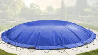 Ein großes rundes Trampolin mit einer Runde aufblasbarem Poolplane steht auf einer Steinterrasse in einem angelegten Garten mit Bäumen und einem Pavillon.