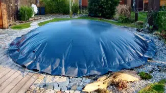 Der Garten verfügt über einen runden, oberirdischen Pool mit einer eleganten runden aufblasbaren Poolplane, umgeben von Steinpflaster, üppigen Pflanzen, hohen Bäumen, einem Holzdeck und einem kleinen Steingarten, der eine ruhige Kulisse bietet.