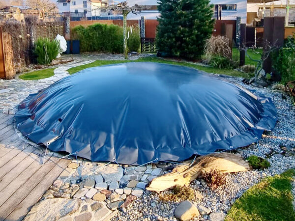 Der Garten verfügt über einen runden, oberirdischen Pool mit einer eleganten runden aufblasbaren Poolplane, umgeben von Steinpflaster, üppigen Pflanzen, hohen Bäumen, einem Holzdeck und einem kleinen Steingarten, der eine ruhige Kulisse bietet.