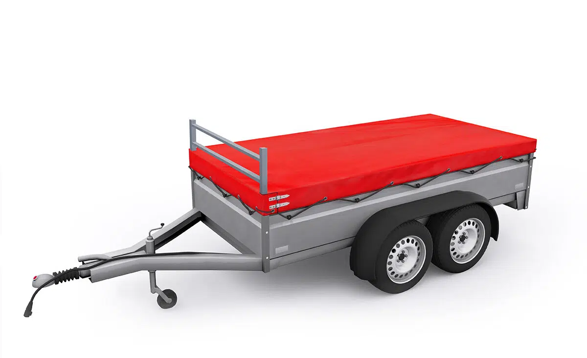 Ein grauer Nutzanhänger mit Doppelrädern und einer roten Anhängerplanen-Abdeckung auf weißem Hintergrund verfügt über eine Anhängerkupplung und einen Metallrahmen und bietet eine stabile Struktur für den mühelosen Transport von Gütern.
