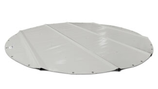 Ein runder Swimmingpool mit teilweise eingefahrener grauer Poolabdeckung, umgeben von einer gemauerten Terrasse. Der Garten bietet üppiges Grün, einen Sonnenschirm und einen Holzzaun mit Sträuchern und Bäumen unter einem blauen Himmel.