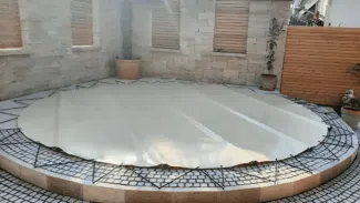 Ein überdachter runder Pool mit runden Poolplanen (Stangenabdeckung) befindet sich auf einer gefliesten Terrasse, umgeben von Pflanzen und modernen Gartenelementen.