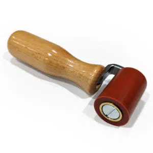 Die Andrückrolle ist ein kleines, handgeführtes Werkzeug mit einem Holzgriff und einem roten Gummirad, ideal zum Andrücken oder Glätten von Oberflächen. Sie ist auf einem weißen Hintergrund abgebildet.