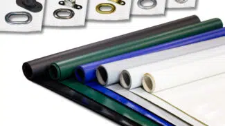 Gerollte PVC-Planenplatten (450 g/m²) in Schwarz, Grün, Blau, Grau und Weiß sind nebeneinander gestapelt, darüber sind auf kleineren weißen Platten Ösen und Befestigungselemente aus Metall und Gummi angebracht.