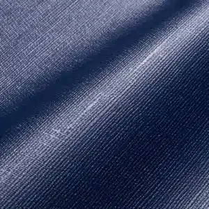 Nahaufnahme eines blauen Denim-Stoffes mit Webstruktur und leichtem Glanz, ähnlich wie MEHGIES® VALMEX® Solera Vorzeltplane. Seine sanften Falten erzeugen weiche Schatten und betonen das Zusammenspiel von Licht und Struktur.