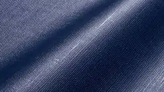 Nahaufnahme eines blauen Denim-Stoffes mit Webstruktur und leichtem Glanz, ähnlich wie MEHGIES® VALMEX® Solera Vorzeltplane. Seine sanften Falten erzeugen weiche Schatten und betonen das Zusammenspiel von Licht und Struktur.