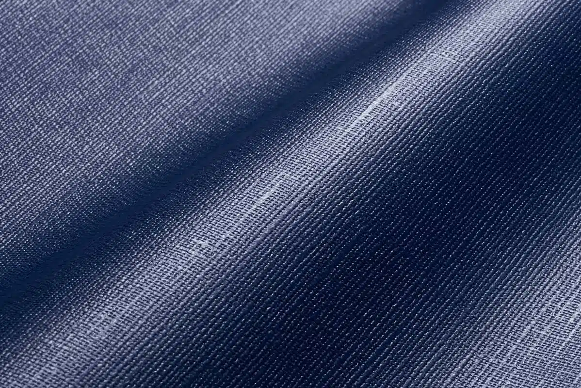 Nahaufnahme eines blauen Denim-Stoffes mit Webstruktur und leichtem Glanz, ähnlich wie MEHGIES® VALMEX® Solera Vorzeltplane. Seine sanften Falten erzeugen weiche Schatten und betonen das Zusammenspiel von Licht und Struktur.