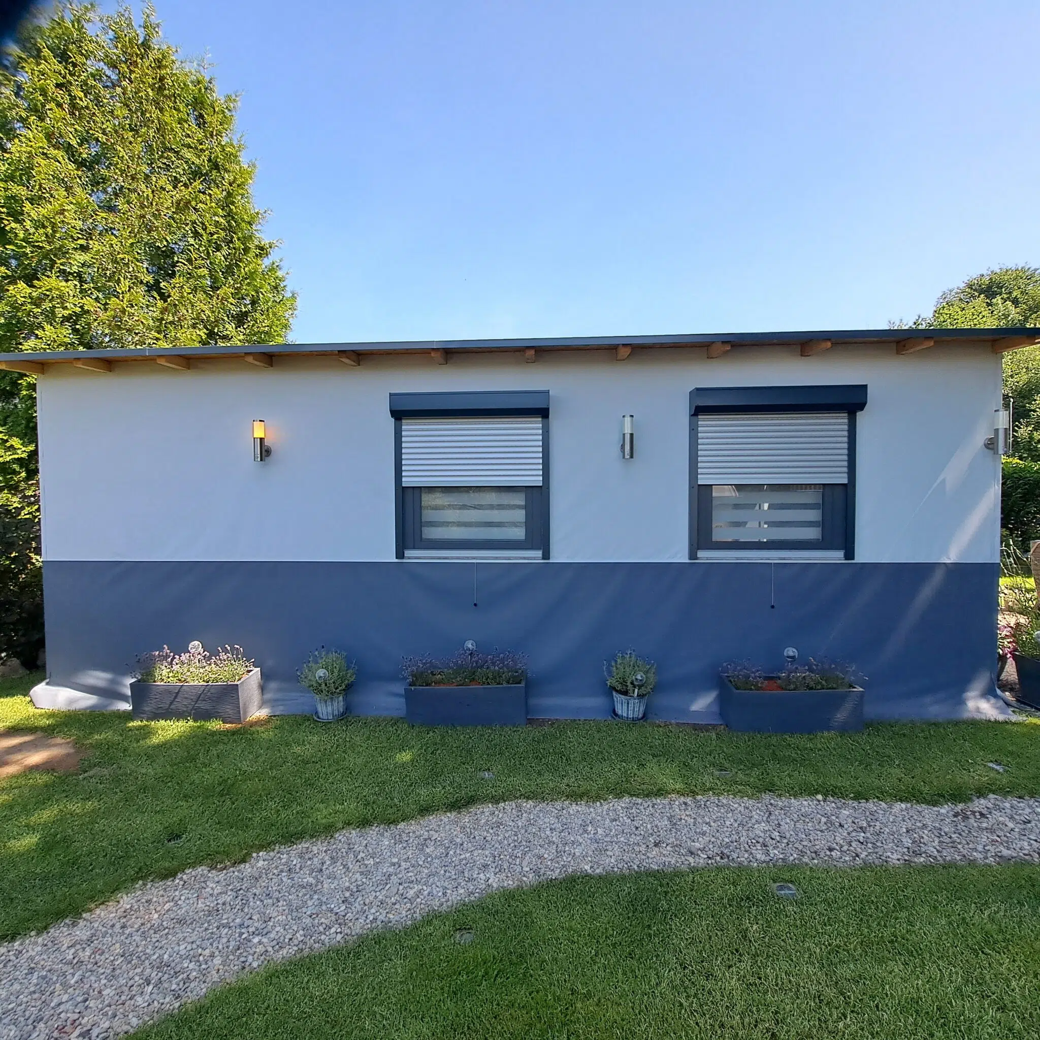 Ein kleines modernes Gebäude - ideal, um die MEHGIES® VALMEX® solera Vorzeltplane - Unifarben (Sondermaß) auf dem grünen Rasen davor zu platzieren.