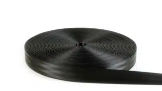 Eine große Rolle Gurtband liegt auf einem weißen Hintergrund, fest aufgewickelt, wobei das lose Ende nach unten rechts ragt. Das schwarze Band weist einen subtilen Glanz und eine gemusterte Textur auf.