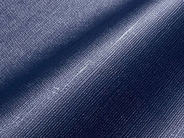 Nahaufnahme eines blauen Stoffes, der an Vorzeltplanen erinnert. Eine diagonale Falte zeigt seine glatte Textur und feine Webart. Die Lichtreflexion hebt seine leicht glänzende Oberfläche und seine satte Farbe hervor.