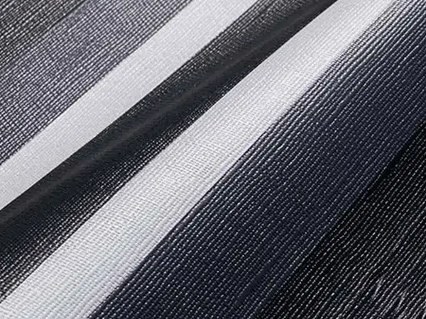 Nahaufnahme einer strukturierten Oberfläche mit diagonalen Streifen in Schwarz, Weiß und Grau, die an Vorzeltplanen erinnert. Das gewebte Muster erzeugt einen sanften Farbverlaufseffekt zwischen den Farben.