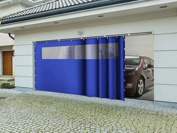 Eine Garage mit einem teilweise geöffneten blauen Schiebeplanentor gibt den Blick auf ein darin geparktes rotes Auto frei. Der Eingang besticht durch ein modernes Design, das durch Kopfsteinpflaster im Außenbereich ergänzt wird.