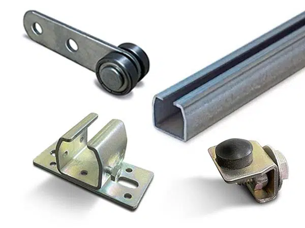 Eine Sammlung von Metallbeschlagkomponenten, darunter eine Rolle mit Halterung, eine hohle Metallschiene, eine Winkelhalterung und ein Klemmstück mit Gummistopper für Schiebeplanen-Systeme.