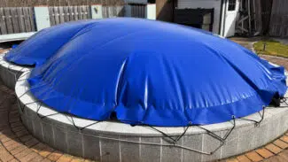 Ein großer, runder Pool ist mit den Achteckigen aufblasbaren Poolplanen abgedeckt, mit Seilen gesichert und auf einer gemauerten Terrasse in einem eingezäunten Hof aufgestellt.