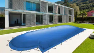 Ein modernes zweistöckiges Gebäude mit großen Fenstern überblickt einen Pool im Hinterhof mit rechteckigen aufblasbaren Poolplanen (+römische Treppe), vor einem grünen Rasen und einer atemberaubenden Berglandschaft.