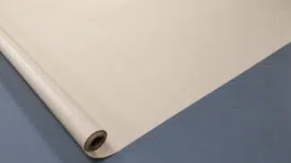 Eine große Rolle cremefarbenen Papiers, teilweise ausgerollt auf einer glatten blauen Oberfläche. Das Papier ist flach ausgebreitet, mit der Rolle auf der linken Seite, wodurch seine glatte Textur und gleichmäßige Farbe sichtbar wird.
