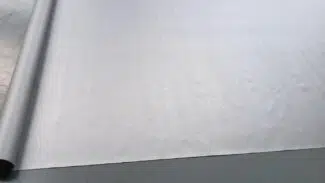 Eine große Rolle hellgrauer Stoff ähnlich dem LKW PVC Planen Reste, teilweise abgerollt mit einer weichen Textur, die subtil Licht einfängt und anmutig geschwungene Kanten hat.