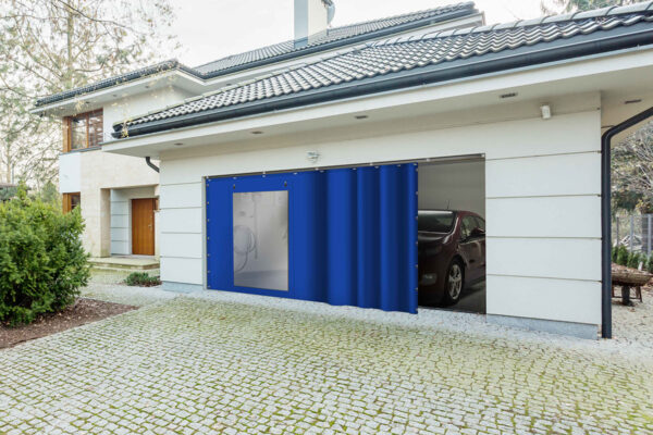 Ein Haus hat eine Garage mit einem blauen Vorhang wie die Schiebeplane mit Fenster/mit Tür, der den Eingang teilweise abdeckt. Im Inneren steht ein geparktes Auto, während die gepflasterte Auffahrt und das Grün einen ruhigen Vordergrund schaffen.