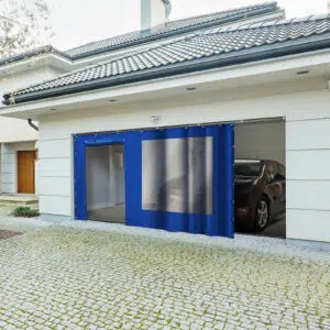 Modernes Haus mit sichtbarer Garage mit Schiebeplane mit Fenster/mit Tür. Im Inneren ist die Vorderseite eines Autos geparkt. Die Außenseite hat ein Ziegeldach, eine gepflasterte Auffahrt und Büsche auf der linken Seite.