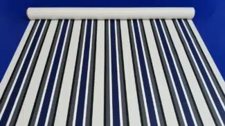 Eine Stoffrolle mit vertikalen Streifen in Marineblau und Weiß ist vor einem einfarbig blauen Hintergrund ausgebreitet.