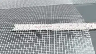 Nahaufnahme eines Maßbandes auf einem gitterförmigen PVC-Netz (550 g/m²) mit kleinen quadratischen Öffnungen. Das 2,18 m breite, hochwertig beschichtete, transluzente PVC-Plane ist mit Maßangaben in Zentimetern abgebildet.