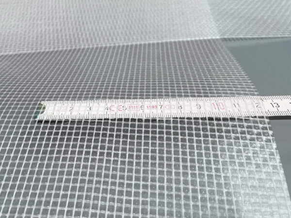Nahaufnahme eines Maßbandes auf einem gitterförmigen PVC-Netz (550 g/m²) mit kleinen quadratischen Öffnungen. Das 2,18 m breite, hochwertig beschichtete, transluzente PVC-Plane ist mit Maßangaben in Zentimetern abgebildet.