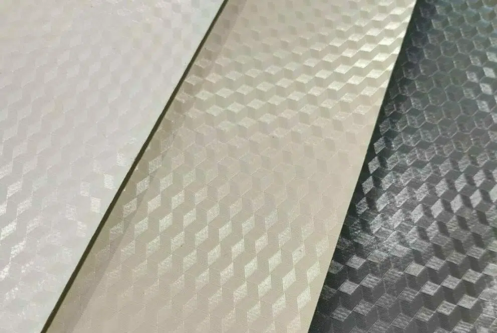 Nahaufnahme von drei strukturierten 3D-Oberflächen mit einem Wabenmuster in Weiß, Beige und Silber, die reflektierende geometrische Designs aufweisen, die der hochwertig beschichteten (850 g/m²) PVC-Folie – 2,5 m breit mit 3D-Prägung – ähneln.