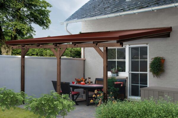 Eine Terrasse mit einer braunen Pergola aus Holz und einer Terrassendachplane an einem Haus mit einem Esstisch, Stühlen, roten Blumen, üppigen grünen Pflanzen und darunter platzierten Sträuchern als Dekoration.