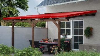 Eine Terrasse mit einem Esstisch im Freien und roten Stühlen unter einer Terrassendachplane ist wunderschön von einem Ziegelweg, Topfpflanzen und üppigem Grün in einem kleinen Garten umgeben.
