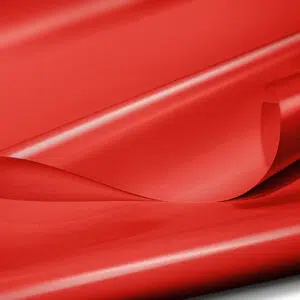 Eine Nahaufnahme des glatten, glänzenden LKW Plane PVC-Gewebes (900 g/m²) in der Farbe Rot RAL3002, leicht zerknittert, sodass seine Struktur und Falten deutlich zu erkennen sind und das Gewebe gleichzeitig Licht reflektiert, das für Glanzlichter und Schatten sorgt.
