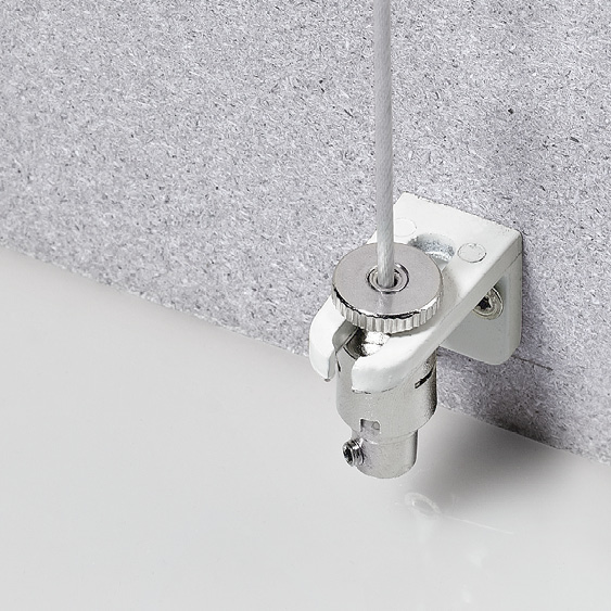 Nahaufnahme einer kleinen Metallhalterung, die an einer weißen Oberfläche befestigt ist und an der ein Kabel befestigt ist, das wie Senkrechtmarkisen vertikal verläuft. Die hellgraue strukturierte Wand bildet einen Kontrast zur glatten Oberfläche.