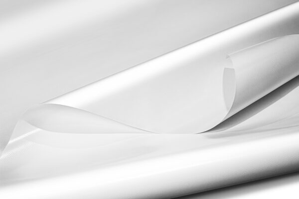Nahaufnahme von übereinander geschichteten weißen, halbtransparenten Kunststofffolien. Die Folien haben eine glatte, glänzende Textur und überlappen sich, wodurch sanfte Falten und ein subtiles Spiel aus Licht und Schatten entstehen.