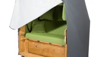 Ein gemütlicher mobiler Unterschlupf aus Holz mit einem grün gepolsterten Sitz und zwei passenden Kissen. Er verfügt über eine grau-weiße Plane und steht auf Rädern, sodass er wie ein tragbares Mini-Zuhause aussieht.