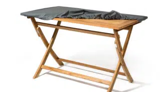 Holztisch mit klappbaren Beinen, dessen Tischplatte teilweise mit einem dunkelgrauen Stoff bedeckt ist. Vor einem schlichten weißen Hintergrund.