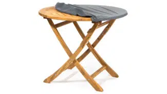 Ein kleiner Klapptisch aus Holz mit gekreuzten Beinen ist teilweise mit einem grauen, drapierten Stoff oder einer grauen Decke bedeckt. Der Tisch steht vor einem schlichten weißen Hintergrund.