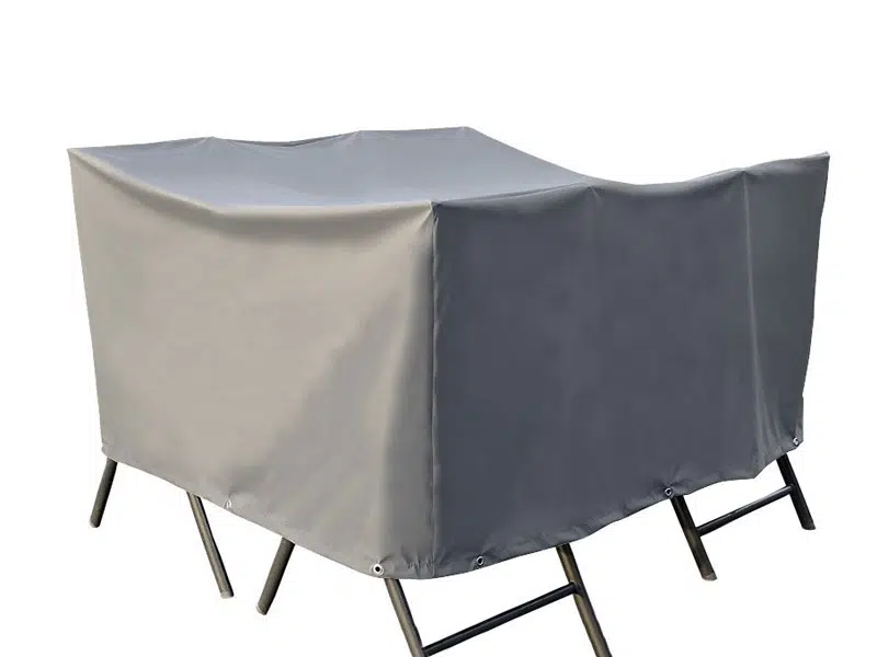 Tisch- und Stuhlset für den Außenbereich, geschützt durch eine graue Abdeckhaube. Die Abdeckung fällt elegant und schützt vor den Elementen, wobei die Möbelstützen darunter dezent sichtbar sind.