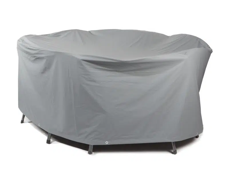 Eine graue Abdeckhauben-Gartenmöbelabdeckung ist über einem runden Gartentisch mit Stühlen angebracht. Sie sitzt unten eng anliegend, gibt aber teilweise die Beine frei.