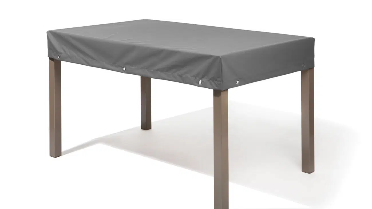 Das Bild zeigt einen rechteckigen Gartentisch mit einer grauen, wasserabweisenden Abdeckung. Die Abdeckung ist mit Ösen an den Ecken versehen. Der Tisch steht vor einem weißen Hintergrund.
