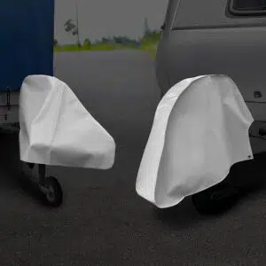 Zwei Anhängerkupplungen, die jeweils mit einer weißen Schutzabdeckung versehen sind, werden auf einer gepflasterten Fläche neben einem Anhänger und einem Wohnmobil abgestellt.