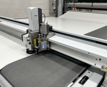 Eine computergesteuerte Stoffschneidemaschine schneidet Material präzise auf einer großen Arbeitsfläche in einer industriellen Umgebung.