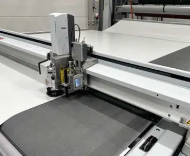 Eine computergesteuerte Stoffschneidemaschine schneidet Material präzise auf einer großen Arbeitsfläche in einer industriellen Umgebung.