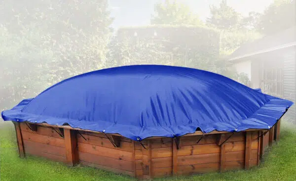 Ein runder, oberirdischer Pool aus Holz ist mit einer leuchtend blauen Plane abgedeckt, die an den Rändern fest verschlossen ist, in einem grasbewachsenen Garten mit Bäumen und einem Schuppen im Hintergrund.