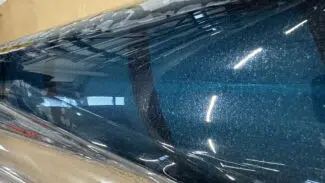 Eine glänzende, reflektierende blaue PVC-Plane/Fensterfolie -Transparent -2.Wahl ruht auf einem Karton und reflektiert Oberlichter und schwache Objekte.